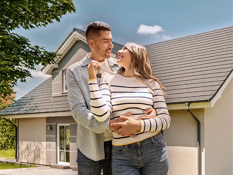 Ein Mann und eine Frau umarmen sich, halten einen Schlüssel in der Hand und stehen vor einem Haus