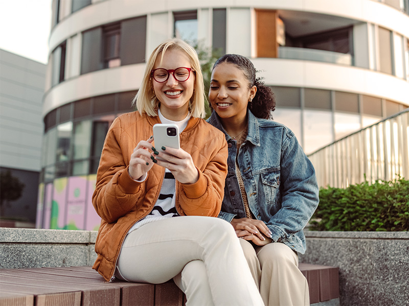 zwei Frauen sitzen auf einer Stufe und schauen auf das Handy