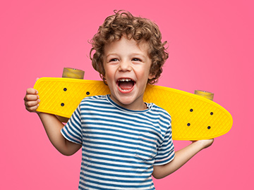 Kleiner Junge trägt Skateboard am Rücken und lacht