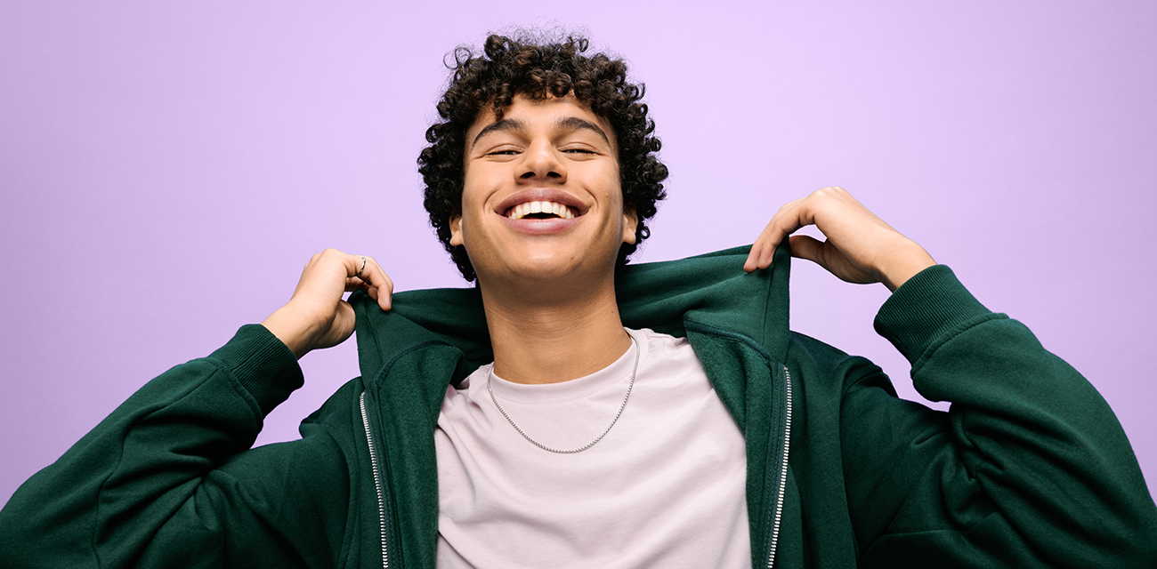 Junge lacht und hält den Kragen seines Hoodies in die Höhe